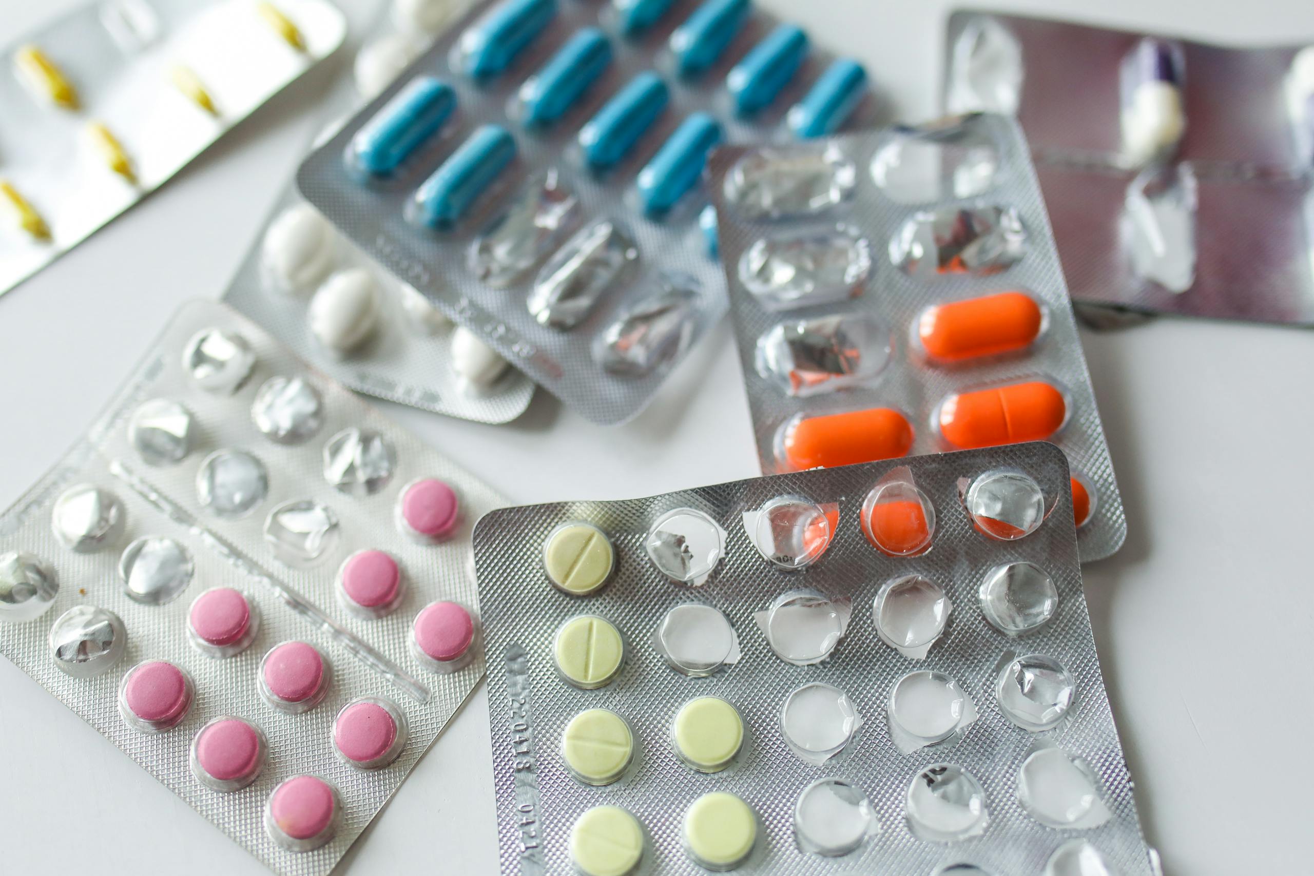 Assorted colorful blister packs of pills and capsules on a white surface.